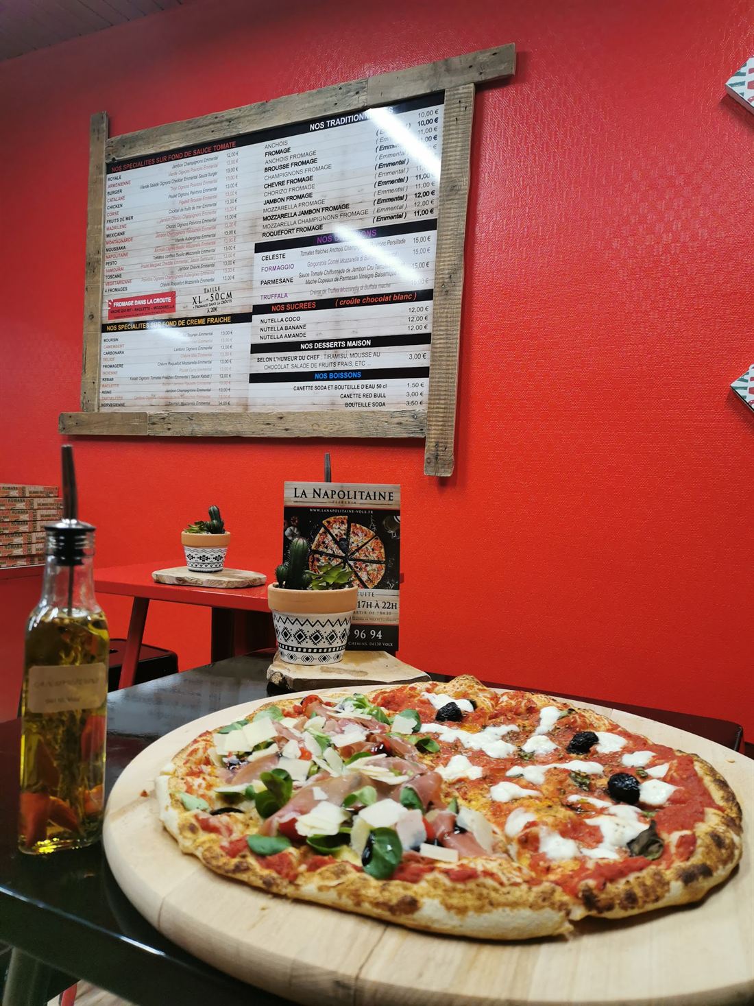 Une pizza posée devant le mur rouge où est affichée la carte