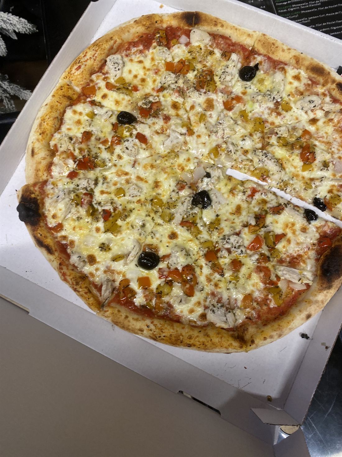 Une pizza dorée aux fromages et aux olives noires, dans sa boîte