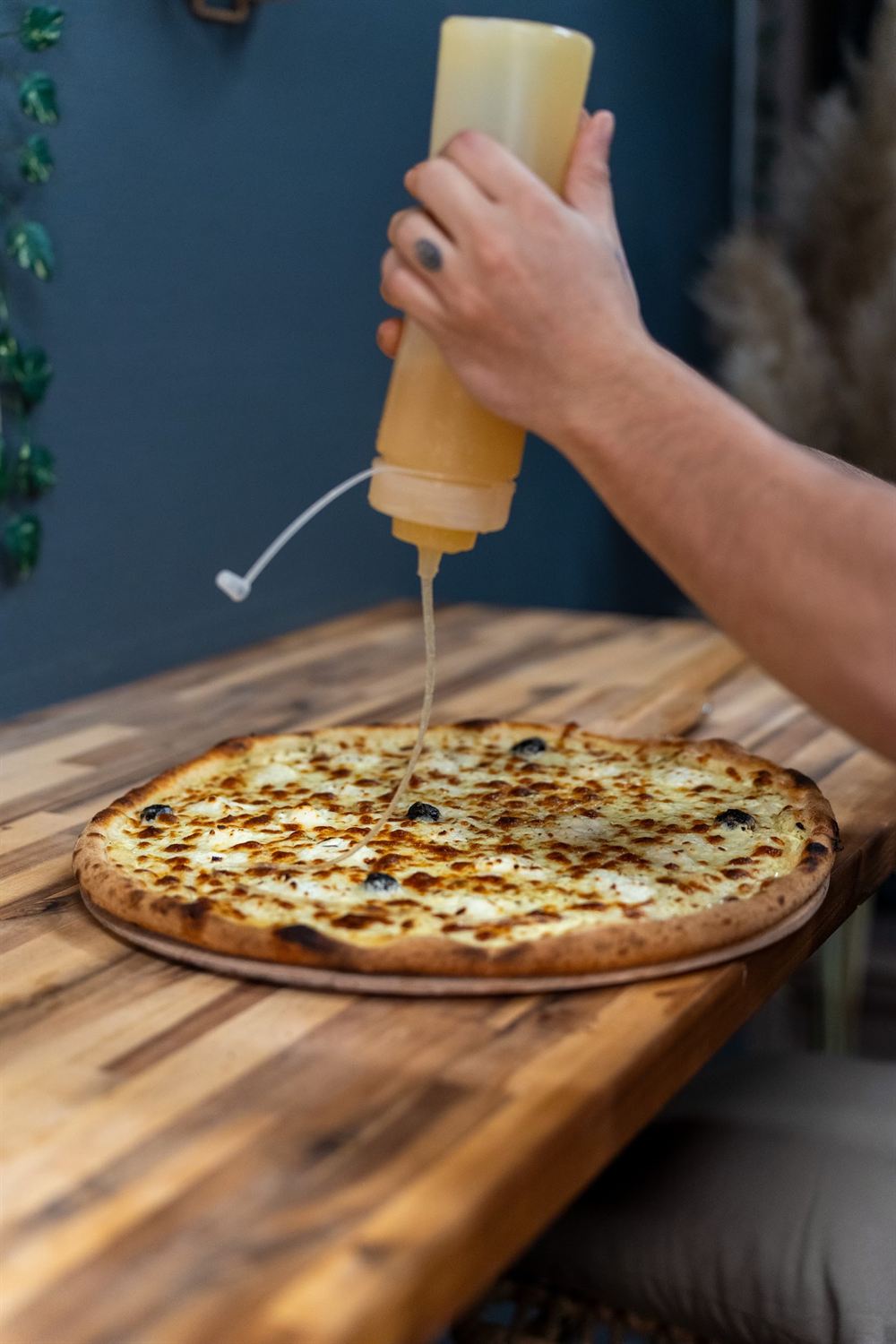 Un filet de sauce versé sur une pizza posée sur un plan de travail en bois